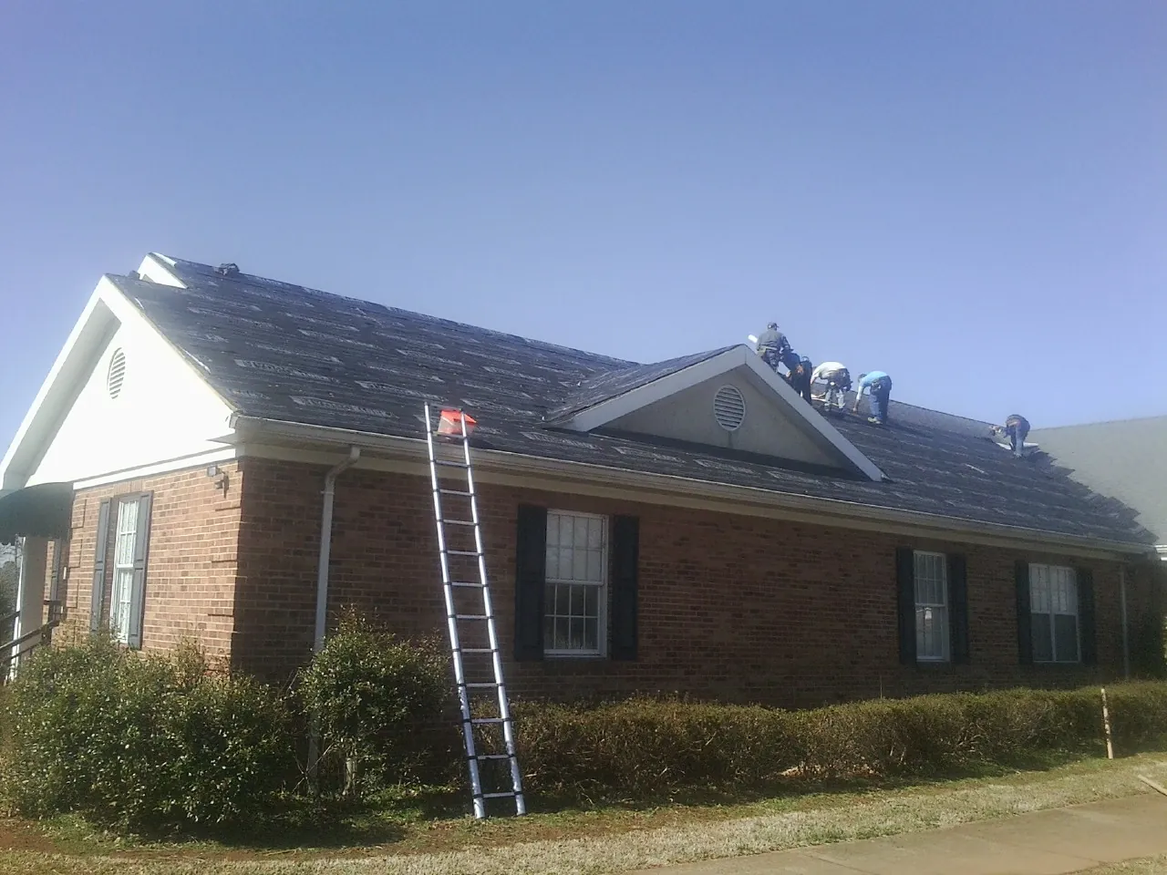 Crew tearing shingles off a brick ranch roof with a ladder set — Emergency Roof Repair work by our crew in Modale