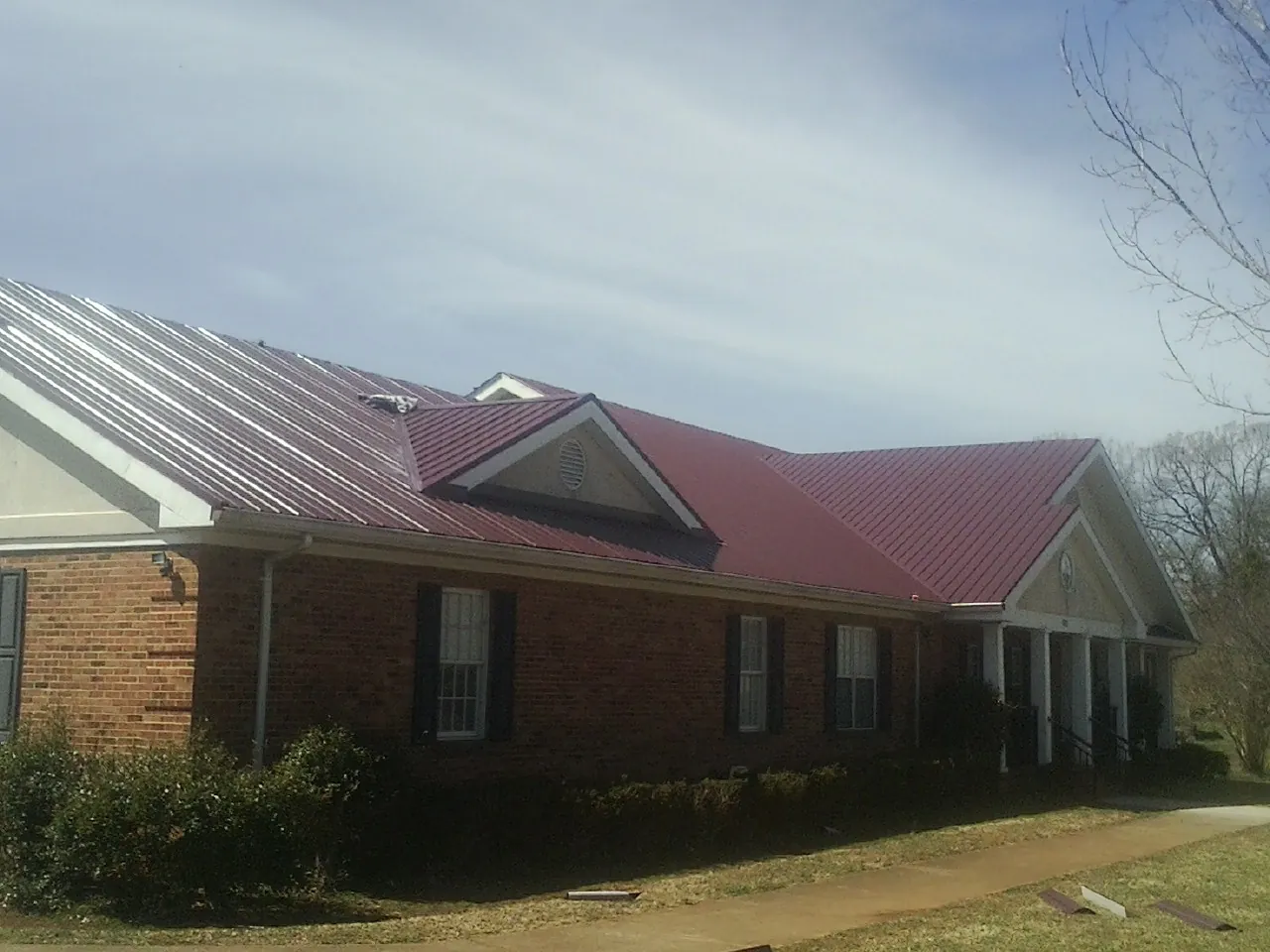 Red metal roof with gabled entries on a long brick building, from a Hail Damage Roof Repair job in Modale