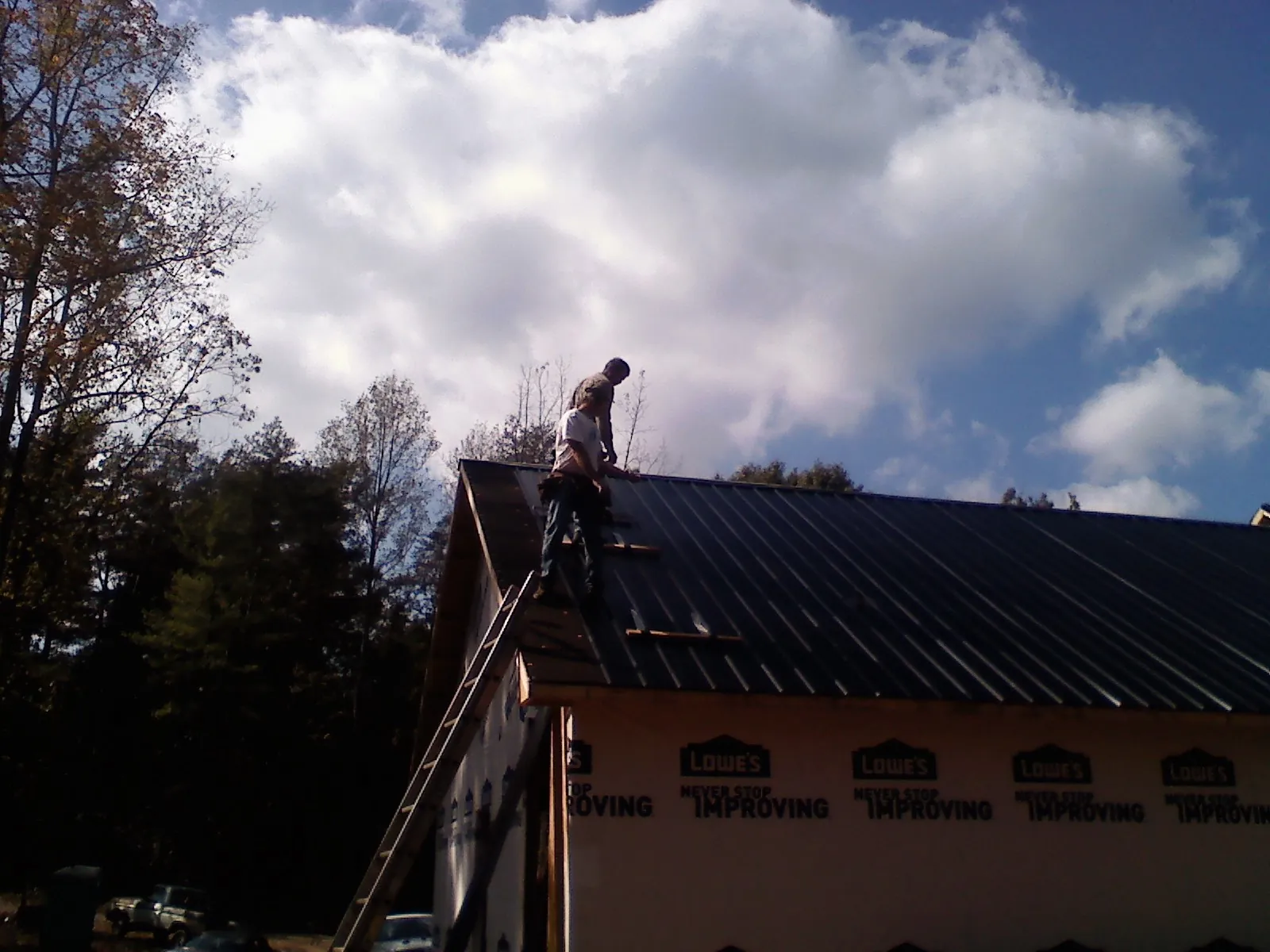 Roofer fastening dark metal panels high against a cloudy sky, from a Roof Inspection job in Modale